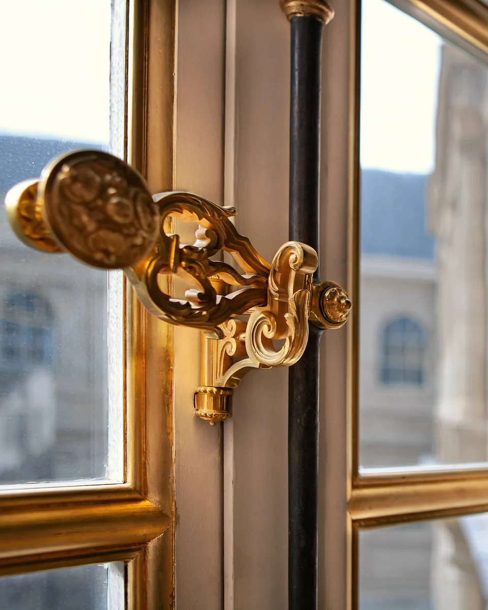 Poignée en bronze doré d’une fenêtre à petits carreaux, boiseries rehaussées d’or